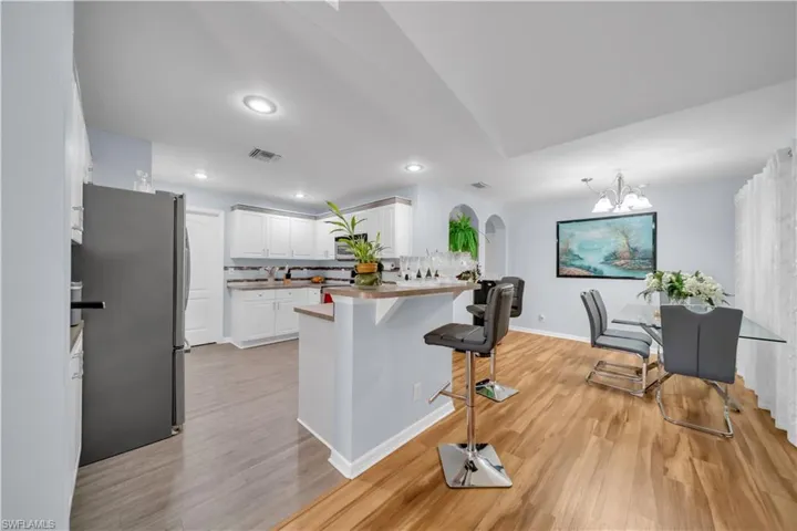 Kitchen with freestanding refrigerator, white cabinets, a kitchen bar, light wood finished floors, and recessed lighting