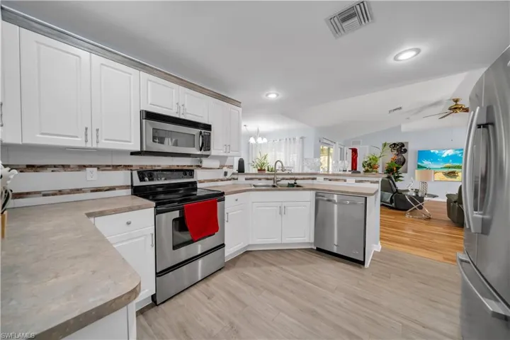 Kitchen featuring appliances with stainless steel finishes, white cabinets, decorative backsplash, lofted ceiling, and light wood-type flooring