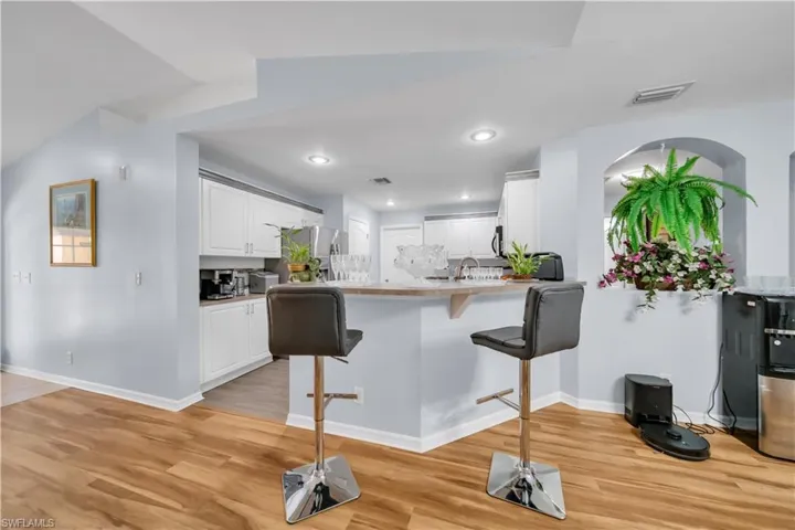Kitchen with a kitchen bar, white cabinetry, backsplash, light wood finished floors, and a peninsula