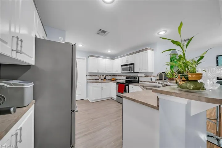 Kitchen featuring appliances with stainless steel finishes, white cabinetry, a peninsula, light wood-style flooring, and backsplash