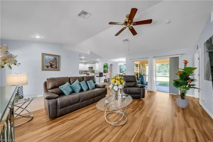 Living room with lofted ceiling, ceiling fan, wood finished floors, and a chandelier