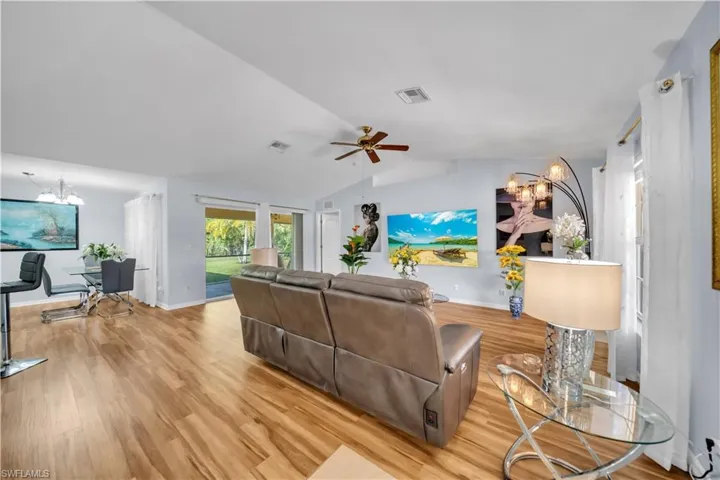 Living area with a chandelier, vaulted ceiling, light wood finished floors, and a ceiling fan