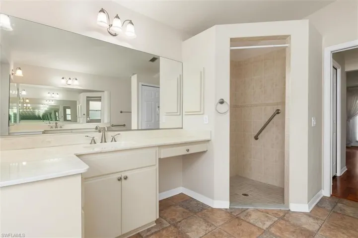Bathroom with vinyl patterned flooring, vanity, and a tile shower