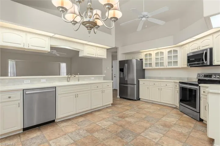 Kitchen with stainless steel appliances, sink, hanging light fixtures, light patterned floors, and ceiling fan with notable chandelier