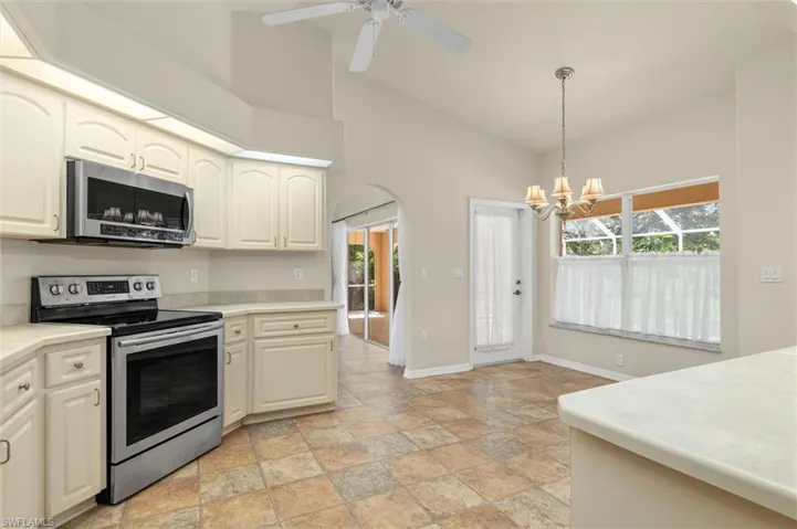 Kitchen with stainless steel appliances, sink, hanging light fixtures, light patterned floors, and ceiling fan with notable chandelier