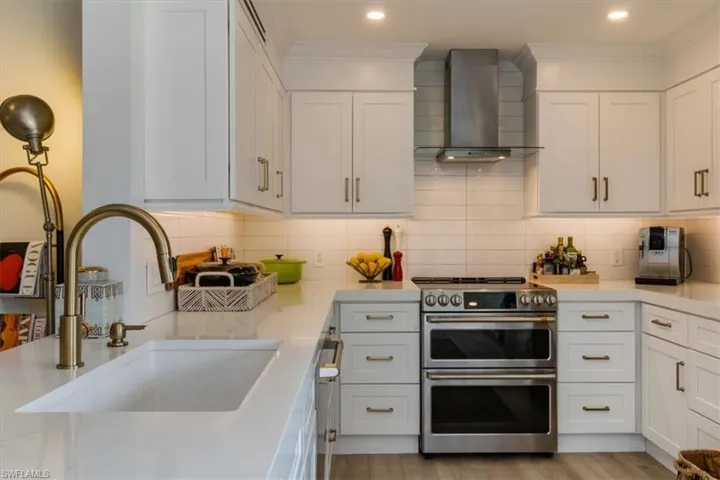 Kitchen with light wood-type flooring, range with two ovens, white cabinets, and wall chimney range hood