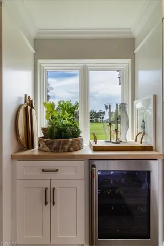 Bar with white cabinetry, wine cooler, and ornamental molding