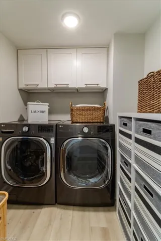 Laundry room featuring light wood-type flooring, cabinets, and washing machine and clothes dryer