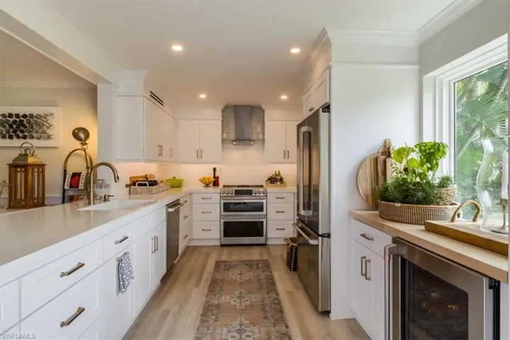 Kitchen with wine cooler, stainless steel appliances, sink, wall chimney range hood, and white cabinets