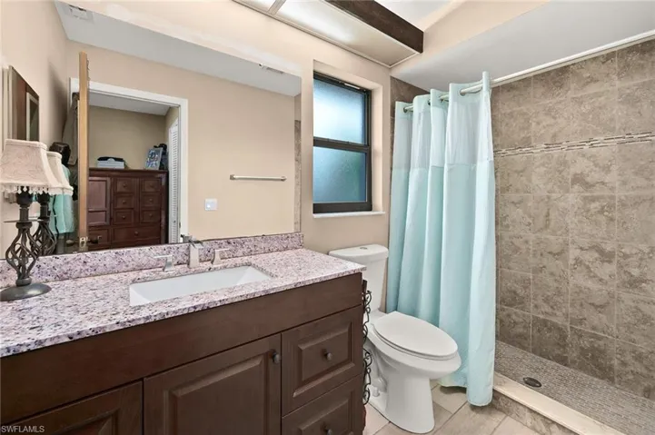 Full bath featuring toilet, vanity, a tile shower, and tile plank patterned floors