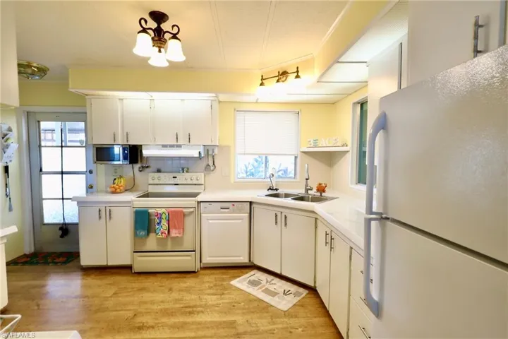 Kitchen with sink, white appliances, white cabinetry, and light wood-type flooring