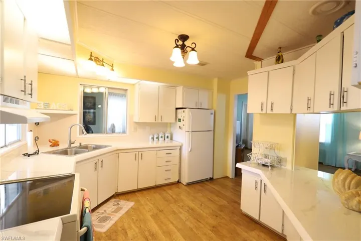 Kitchen featuring white fridge, light wood-type flooring, stove, sink, and white cabinets