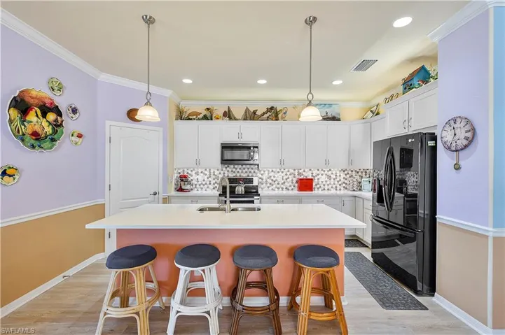 Kitchen featuring white cabinetry, black fridge, hanging light fixtures, and an island with sink