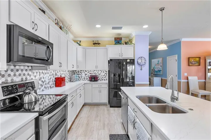 Kitchen with sink, stainless steel appliances, backsplash, decorative light fixtures, and white cabinets