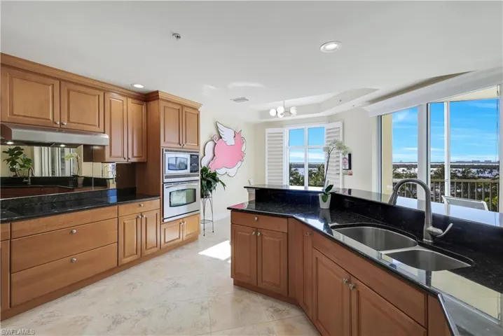 Kitchen featuring appliances with stainless steel finishes, a notable chandelier, dark stone counters, and sink
