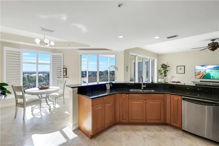 Kitchen featuring ceiling fan with notable chandelier, sink, dark stone countertops, dishwasher, and plenty of natural light