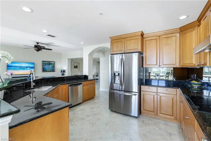 Kitchen featuring sink, ceiling fan, dark stone countertops, kitchen peninsula, and stainless steel appliances