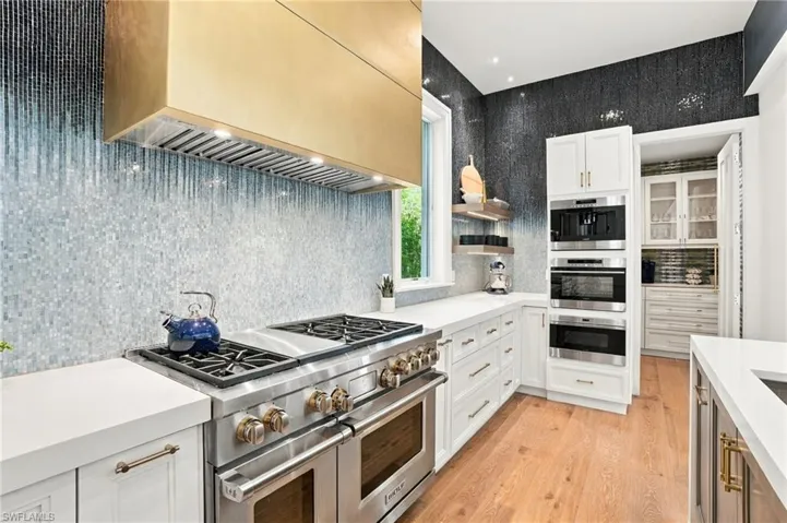 Professional-grade stainless steel range with a brass-finish range hood, white cabinetry, integrated stainless steel wolf appliances