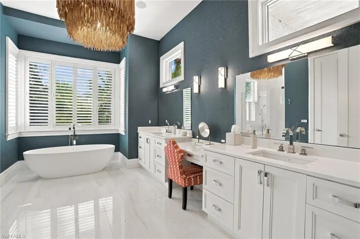 White freestanding soaking tub, dual vanities and abundant natural light through the transom windows with a decorative chandelier