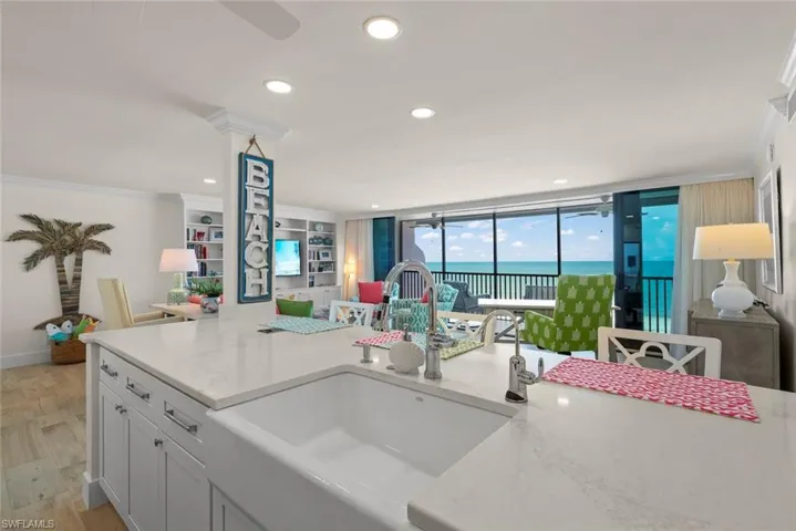 Kitchen island featuring a farmhouse sink and light-toned countertop, with open-concept living area and floor-to-ceiling sliding glass doors