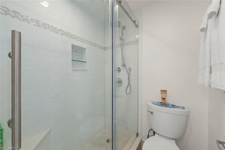 Glass-enclosed shower featuring white subway tile, a decorative mosaic tile accent band, and a built-in shower niche with a glass shelf