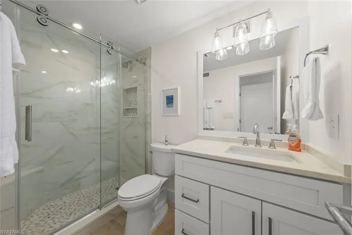 Bathroom featuring a walk-in shower with a glass sliding door, stone pebble floor, and marble-look tile surround