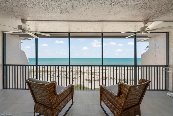 Screened balcony featuring direct beachfront exposure, tile flooring, and two ceiling fans