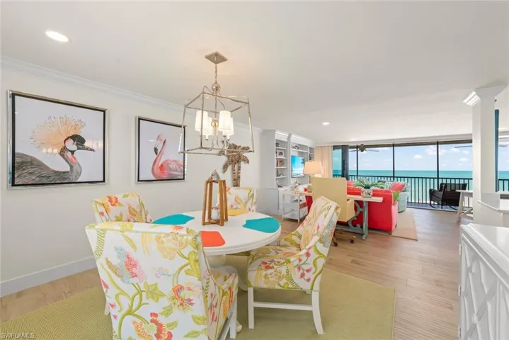 Open-concept living space featuring wood-finish flooring, built-in shelving, a full wall of glass overlooking the ocean, and a recessed ceiling with crown molding