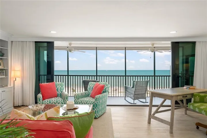Living area featuring floor-to-ceiling sliding glass doors, light wood-finish flooring, a built-in wall unit with display shelving, recessed lighting, and direct access to an outdoor balcony with water views