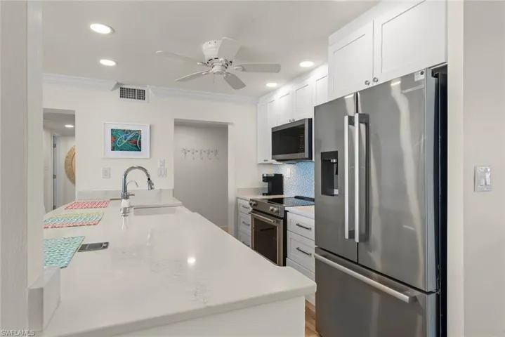 Modern kitchen featuring a large island with a sink, white shaker cabinetry, stainless steel appliances, and a tiled backsplash