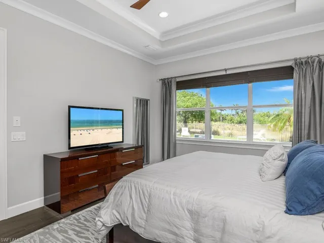 Bedroom with wood finished floors, a tray ceiling, crown molding, recessed lighting, and baseboards