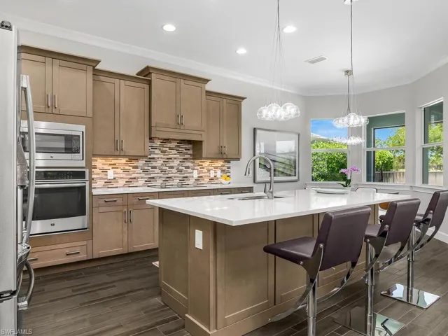 Kitchen featuring stainless steel appliances, a sink, quartz countertops, backsplash, and a kitchen breakfast bar