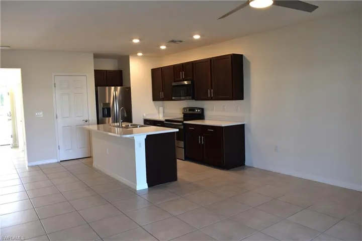 Kitchen with dark wood finish cabinets, stainless steel appliances, light countertops, a center island with sink, and recessed lighting