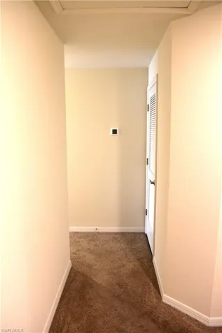 Hall featuring dark colored carpet and baseboards
