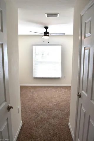 Spare room with ceiling fan and dark colored carpet
