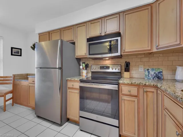 Kitchen with tasteful backsplash, light stone countertops, light tile patterned flooring, and stainless steel appliances