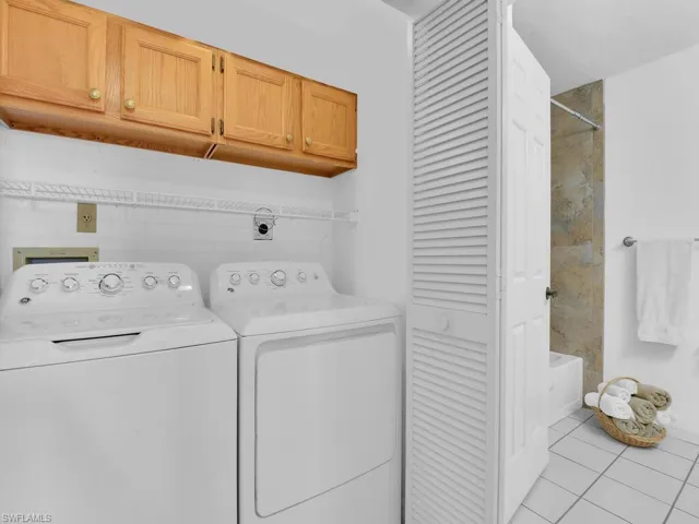 Laundry room with washing machine and clothes dryer, light tile patterned floors, and cabinets