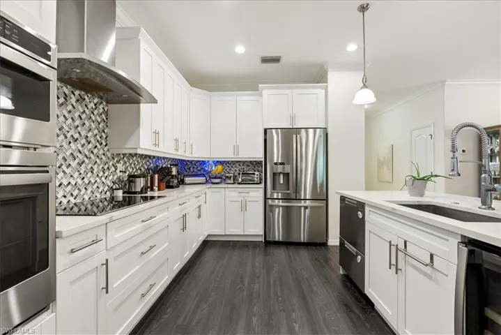 Kitchen featuring appliances with stainless steel finishes, light countertops, wall chimney exhaust hood, ornamental molding, and tasteful backsplash