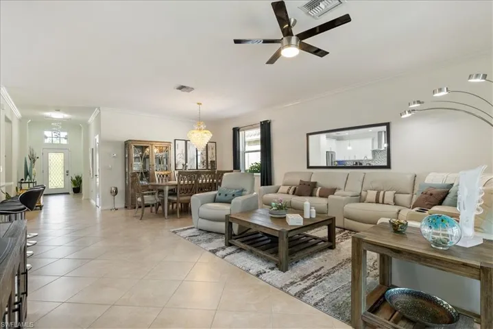 Living area with ornamental molding, light tile patterned floors, a ceiling fan, and a chandelier