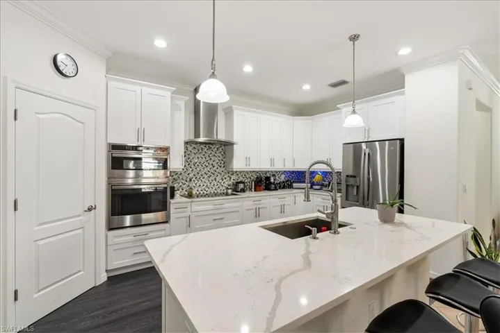 Kitchen featuring appliances with stainless steel finishes, tasteful backsplash, a breakfast bar, wall chimney range hood, and white cabinets