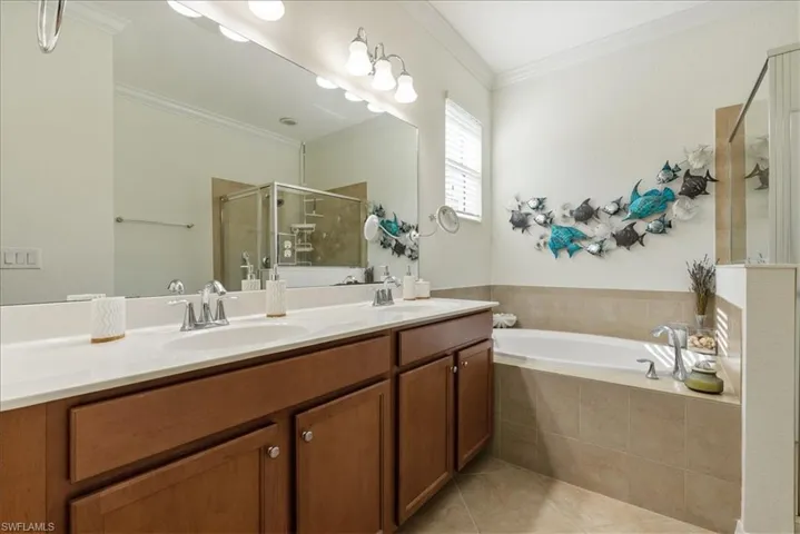 Bathroom with double vanity, a stall shower, a garden tub, tile patterned flooring, and crown molding