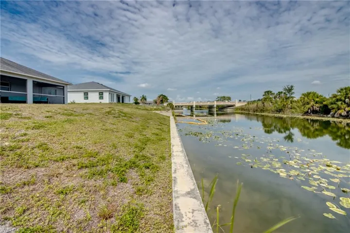 Waterfront property featuring a concrete seawall, natural water vegetation, a screened-in patio, and a concrete bridge