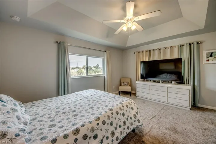 Bedroom featuring a tray ceiling, ceiling fan with integrated lighting, and carpet flooring