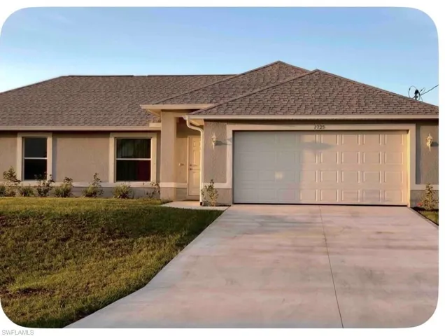 Stucco exterior featuring an attached two-car garage with a panel door, a concrete driveway, a gabled shingle roof, and a minimal landscaping design with shrubbery