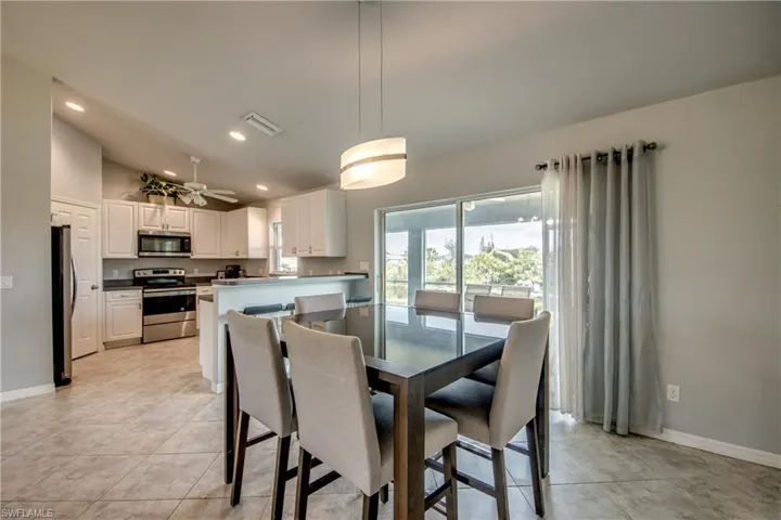 Bright kitchen and dining area featuring white cabinetry, stainless steel appliances, a breakfast bar, and sliding glass doors