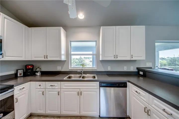 Kitchen featuring abundant white cabinetry, dark countertops, a double basin stainless steel sink, and a stainless steel dishwasher