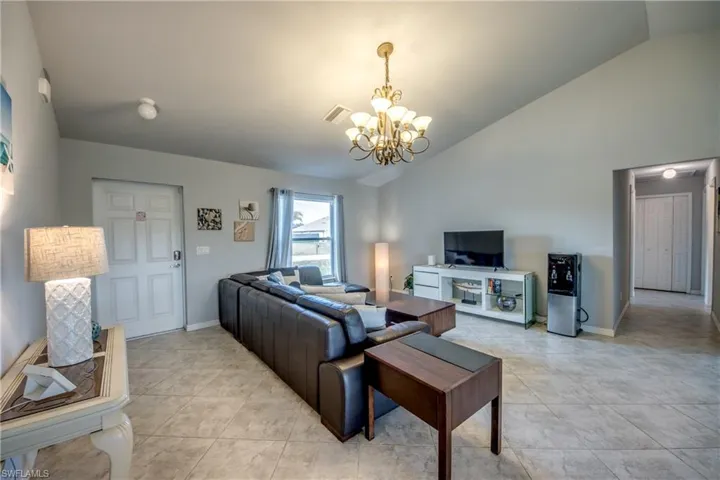 Spacious living area featuring vaulted ceilings, tile flooring, a window with horizontal blinds, and a decorative chandelier