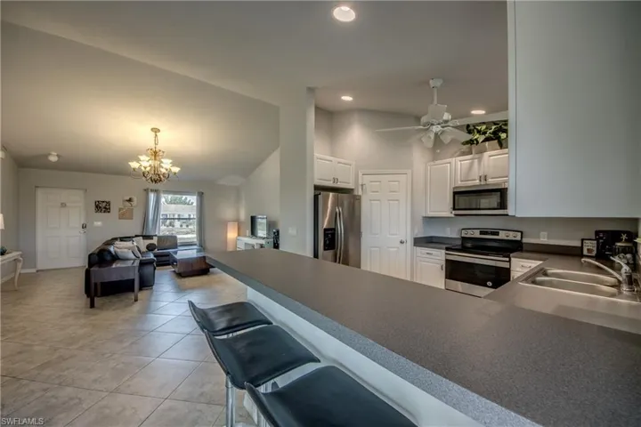 Open-concept living space featuring a kitchen with white cabinetry, stainless steel appliances, a breakfast bar, and tile flooring