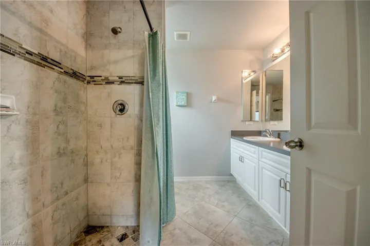 Full bathroom featuring a tiled shower with decorative accent band, a single vanity with storage cabinetry, a framed mirror, and tile flooring