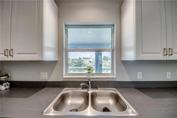 Dual basin stainless steel sink set within a dark countertop, framed by white upper cabinetry with brushed nickel hardware